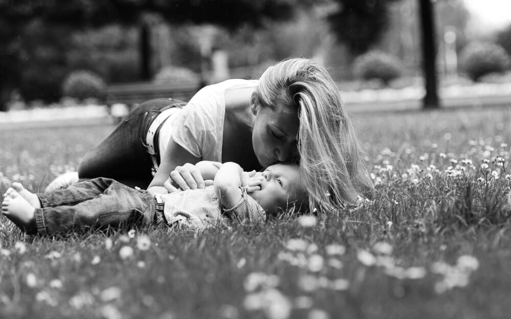 Mama liegt mit Baby in den Gänsblümchen im Park. (www.susannewatrin.de)