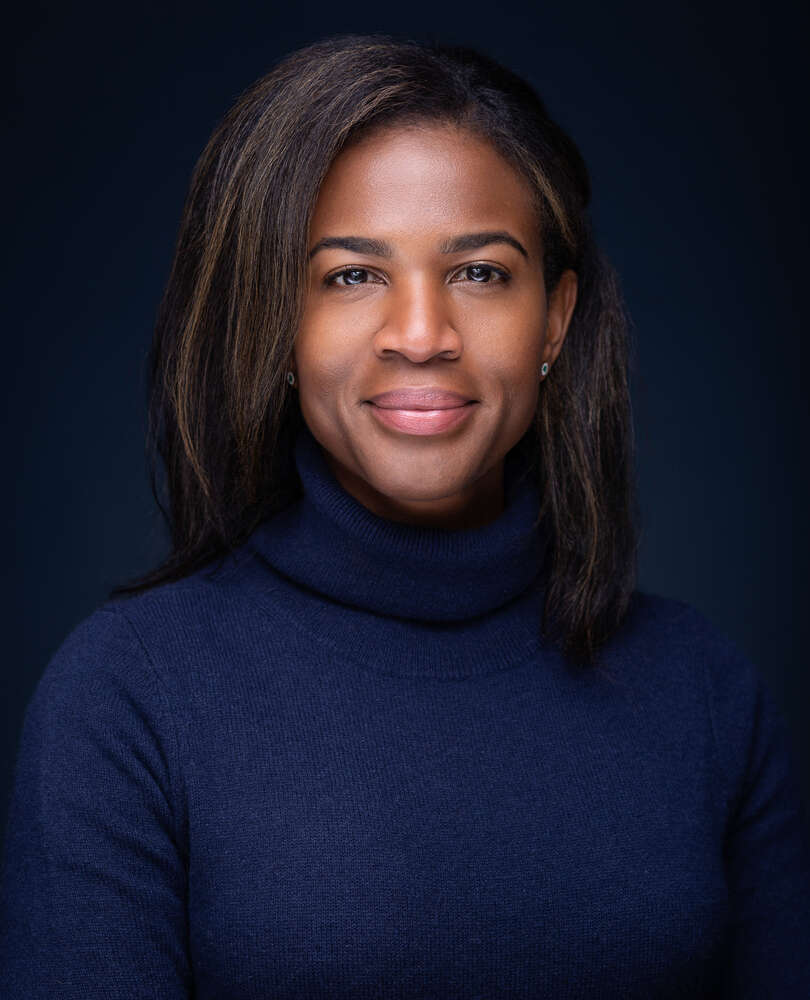 Porträt einer Frau, vor einem dunklen Hintergrund mit einem blauen Pullover. (Headshot Master)