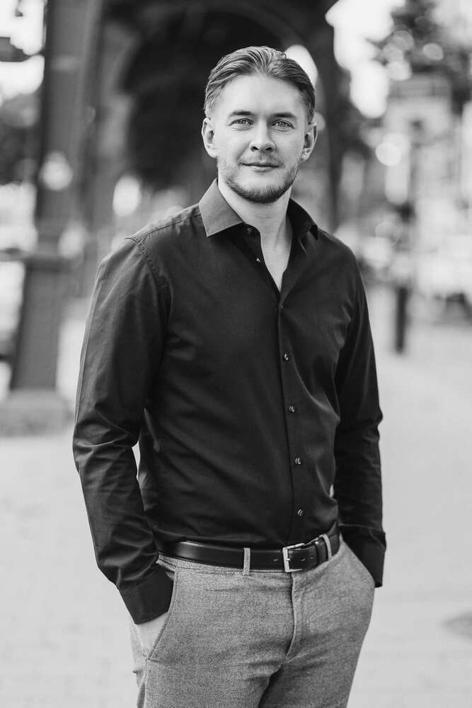 Lächelnder junger Berufstätiger im Freien in einem schwarzen Hemd, offenes Schwarz-Weiß-Porträt (Headshot Master)