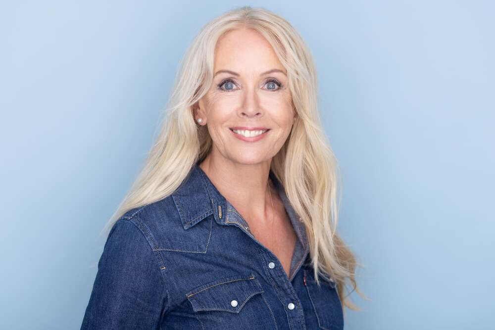 Porträt einer lächelnden Frau in Jeanshemd vor zartblauem Hintergrund. (Headshot Master)