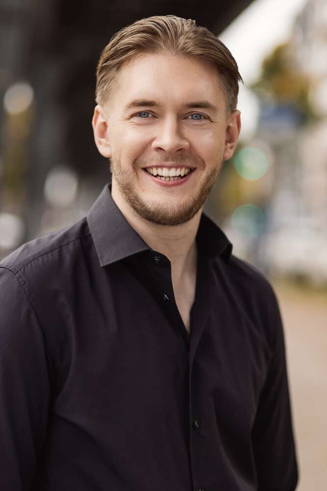 Lächelnder junger Mann im Freien in einem schwarzen Hemd, offenes Porträt (Headshot Master)