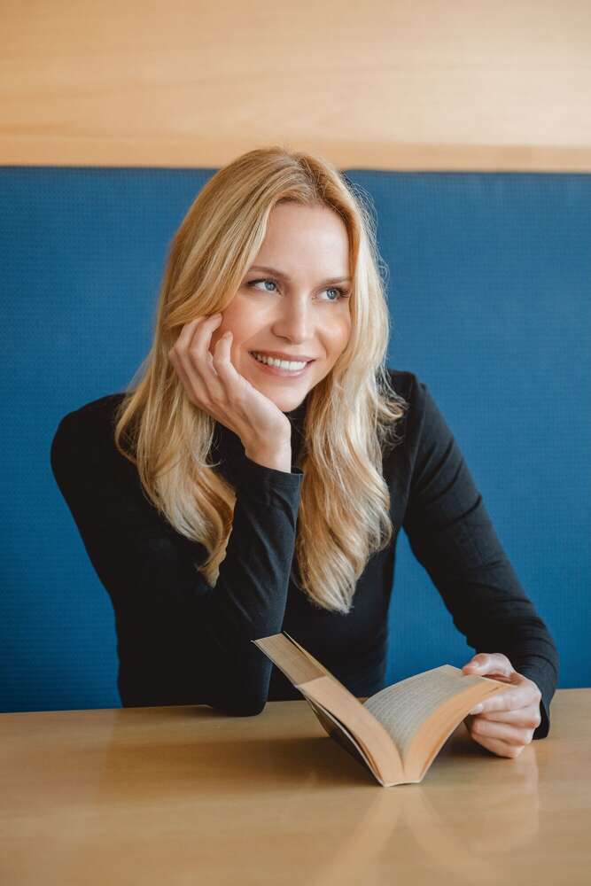 Portrait einer sitzenden, lächelnden blonden Frau die ein Buchg liest   (Axel Jahnke | Fotografie)