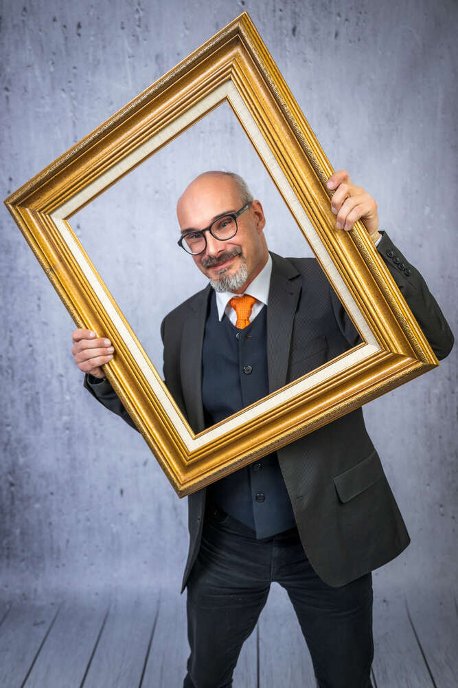 Mann im Anzug schaut durch einen selbst gehaltenen goldenen Bilderrahmen  (Axel Jahnke | Fotografie)
