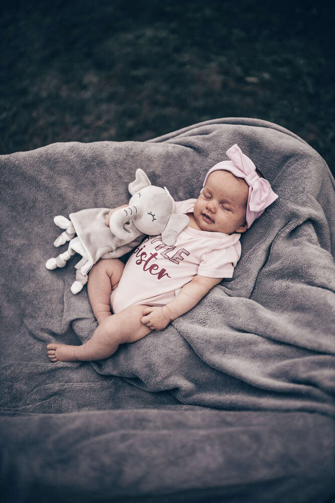 Neugeborenenfoto „Little Sister“ auf grauer Decke (FOKUSNAH)