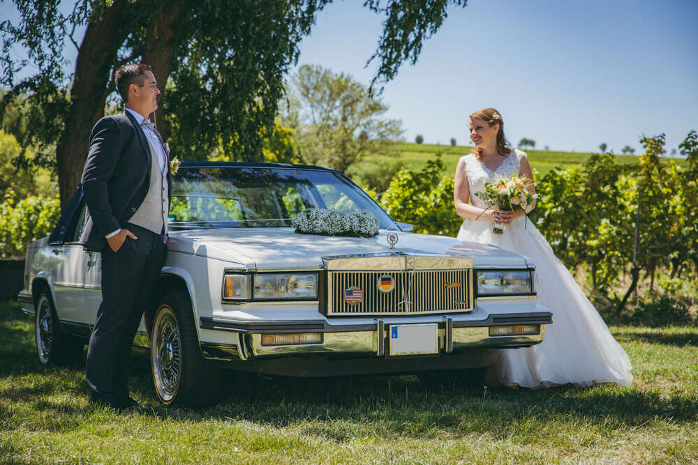 HOCHZEITSPAAR MIT WEISSEM CADILLAC IN DEN WEINBERGEN BEI SONNENSCHEIN (FOKUSNAH)